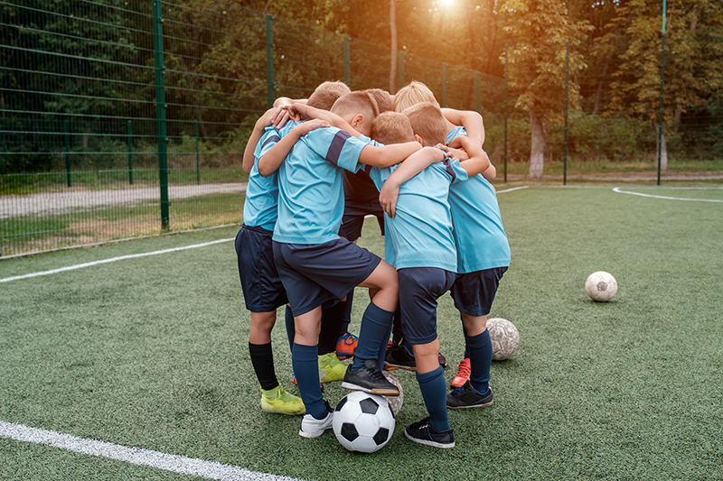 Children soccer team and coach hugs each other on football field before match outdoors at summer